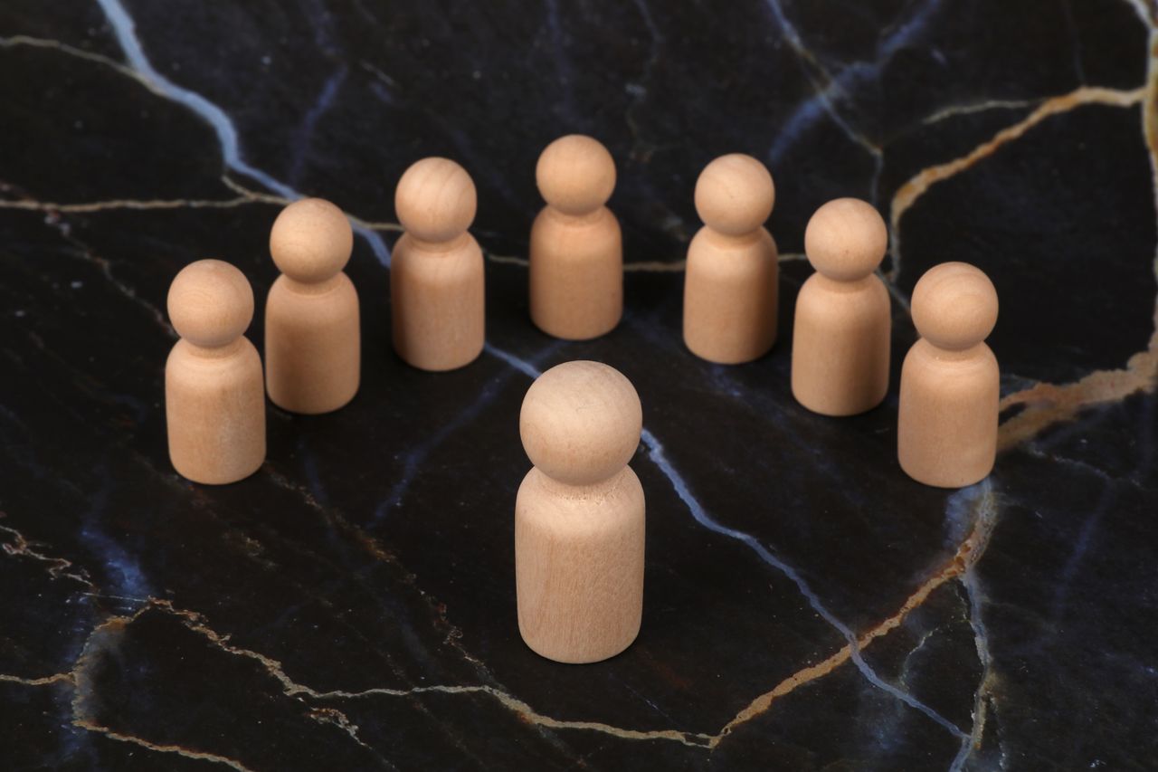 Home Wooden human figures arranged on a dark marble background depicting leadership or teamwork.