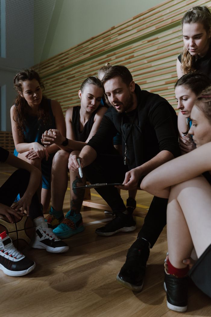 Home Basketball coach discusses strategy with female team indoors, focusing on teamwork and game planning.